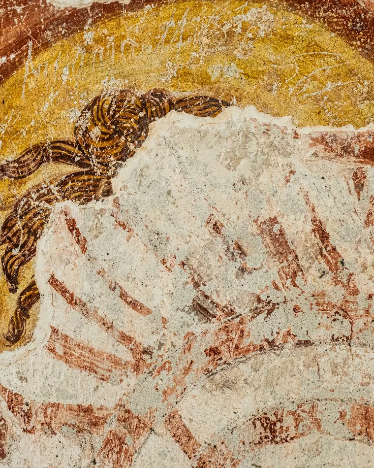 Detalle de un fresco antiguo con una figura nimbada y la superficie del mortero desgastada